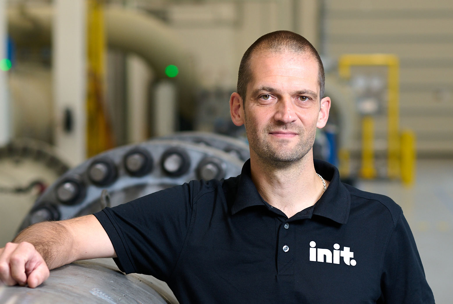 Man leaning against a large pipe. He is wearing black t-shirt with Init logo looking into the camera